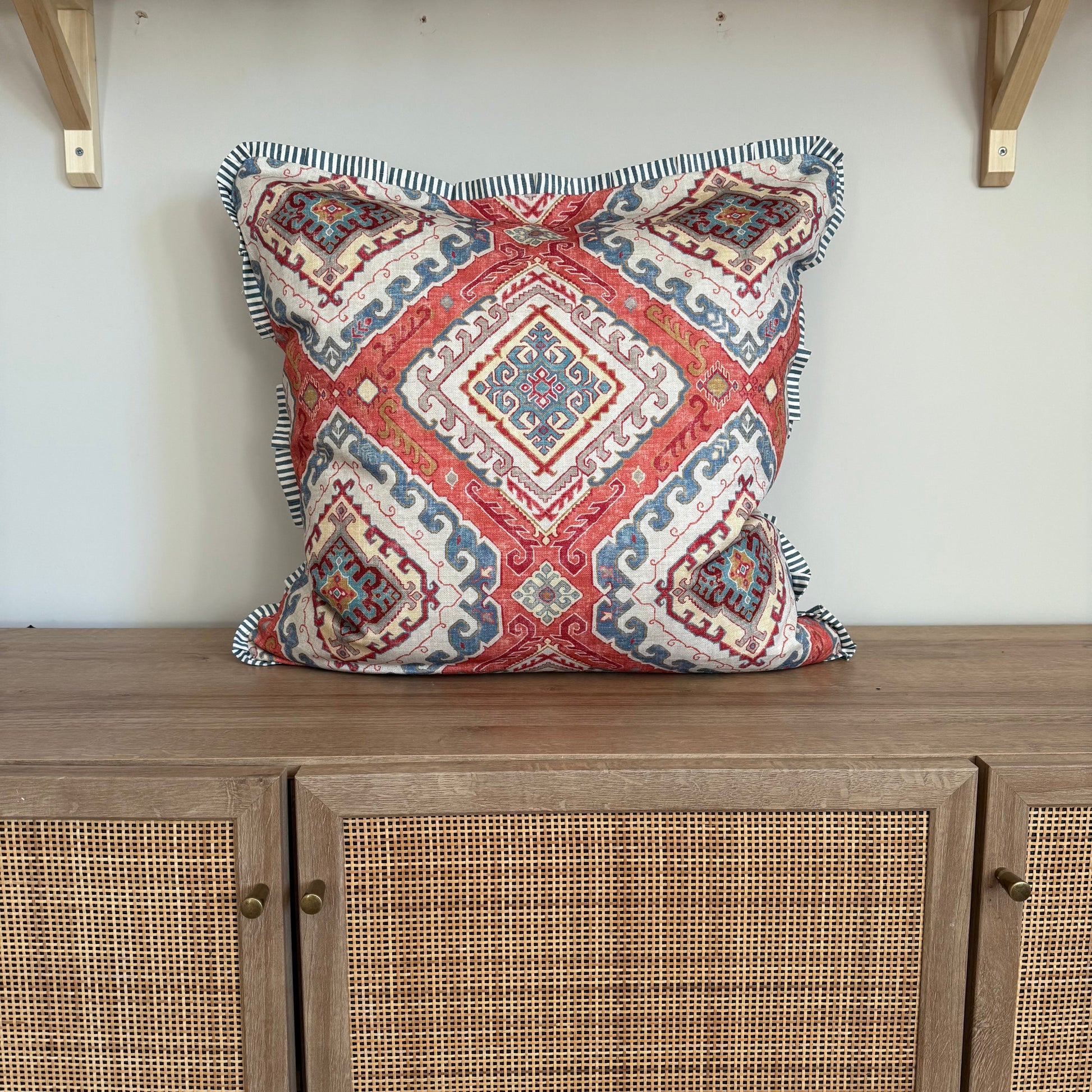 Decorative pillow with geometric pattern on a white wall next to wooden furniture.