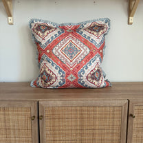 Decorative pillow with geometric pattern on a white wall next to wooden furniture.
