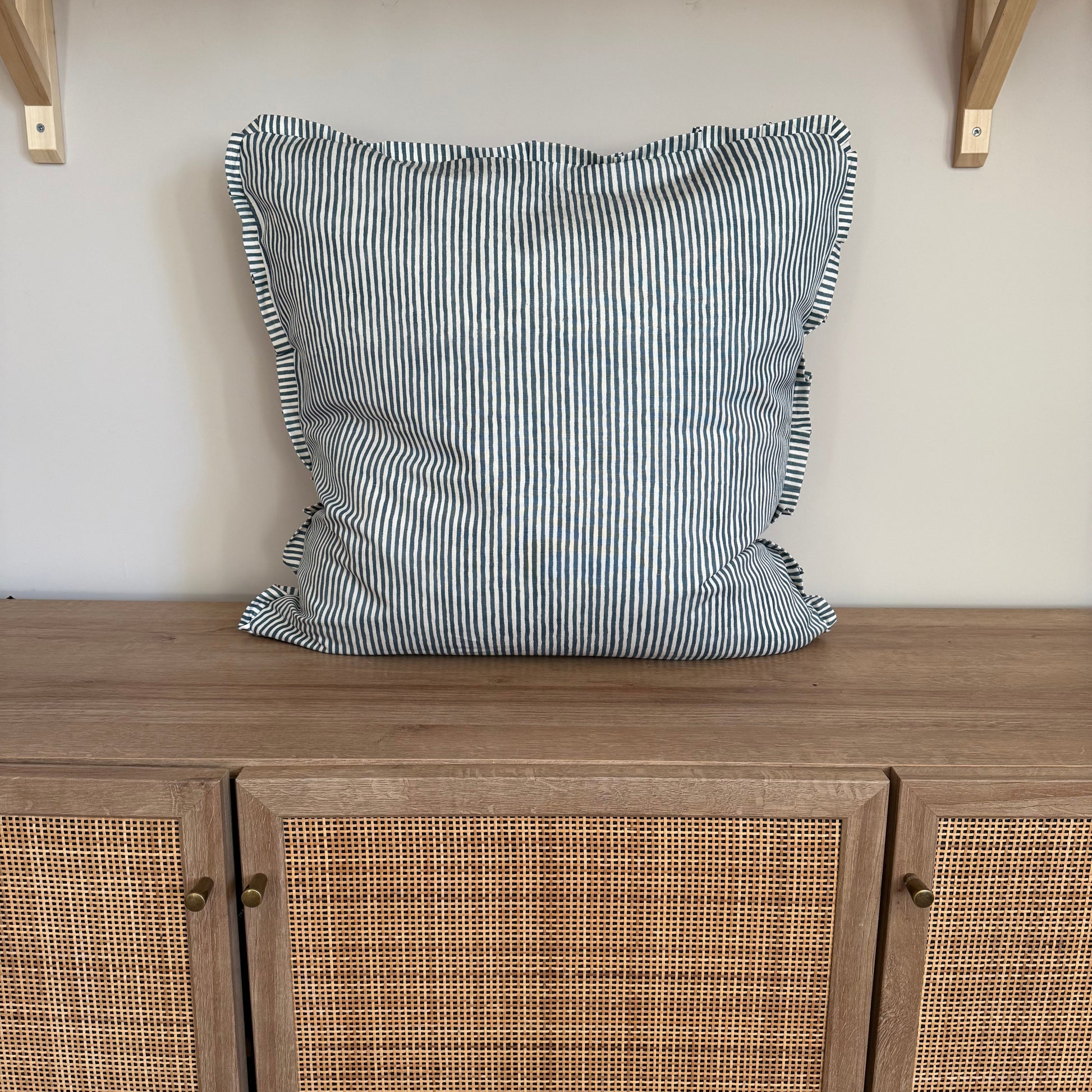 Striped pillow on a wooden cabinet with rattan doors.