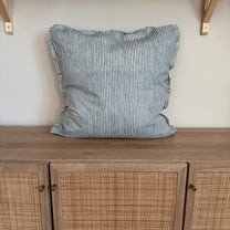 Striped pillow on a wooden cabinet with rattan doors.
